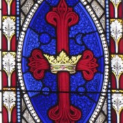 At the center of the lancets, in an oval medallion with a bright blue background, is a red cross with a gold crown, symbolizing Jesus’ Crucifixion and Resurrection as King of Heaven. The red-ground medallions radiating from it represent the ways the benefits of Christianity are communicated: