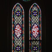 Set into the grisaille are often medallions in bright blue, red, and other colors, decorated not with scenes of Biblical stories as in many churches, but with symbols of religious significance and with words—often quotations from the Bible. This style of window was commonly employed in English parish churches of the thirteenth century. Since Grace Church’s architecture imitates churches like these, the windows appropriately complement the building. Grisaille serves to screen out some of the outdoor light, but not as much as the deeply colored glass popular in earlier Gothic architecture, particularly in France.